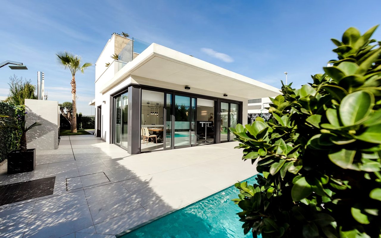 Modern white home with glass doors, a turquoise pool, and tropical landscaping.