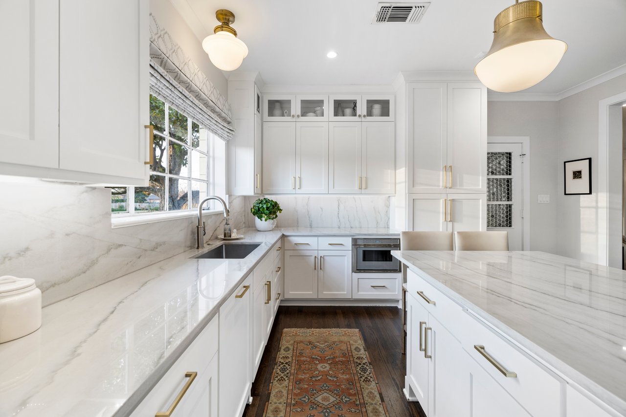 white marble counters in updated kitchen with white cabinets and dark hardwood floors