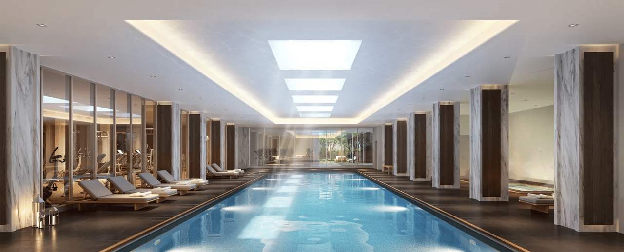 Indoor pool with marble columns, lounge chairs, skylights, and a fitness room behind glass walls.