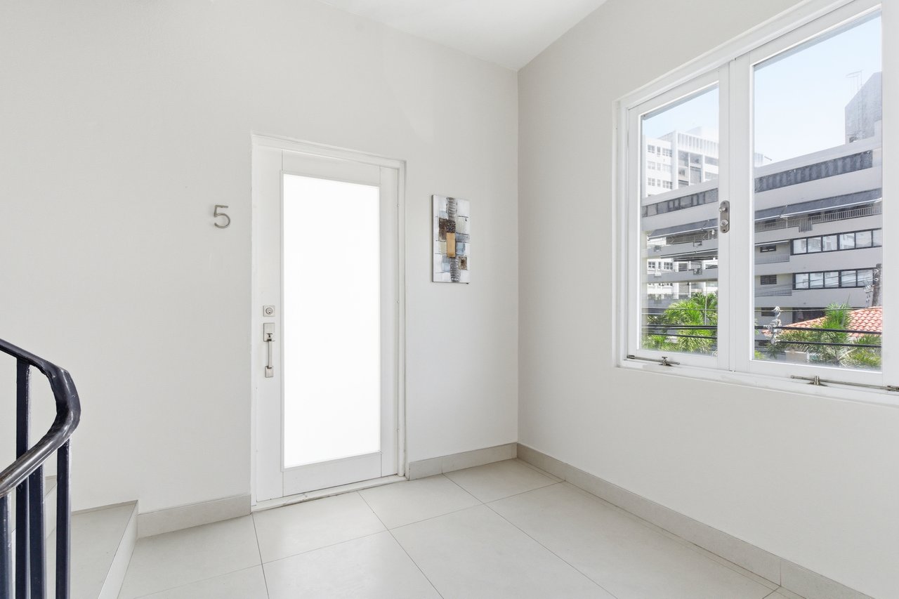 Vacant tiled entry hall with a door marked 5, large window, and curved stair railing.
