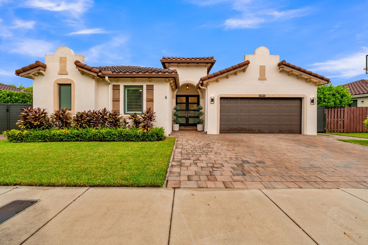 Stucco house with a tiled roof, arched entry, two-car garage, and paver driveway.