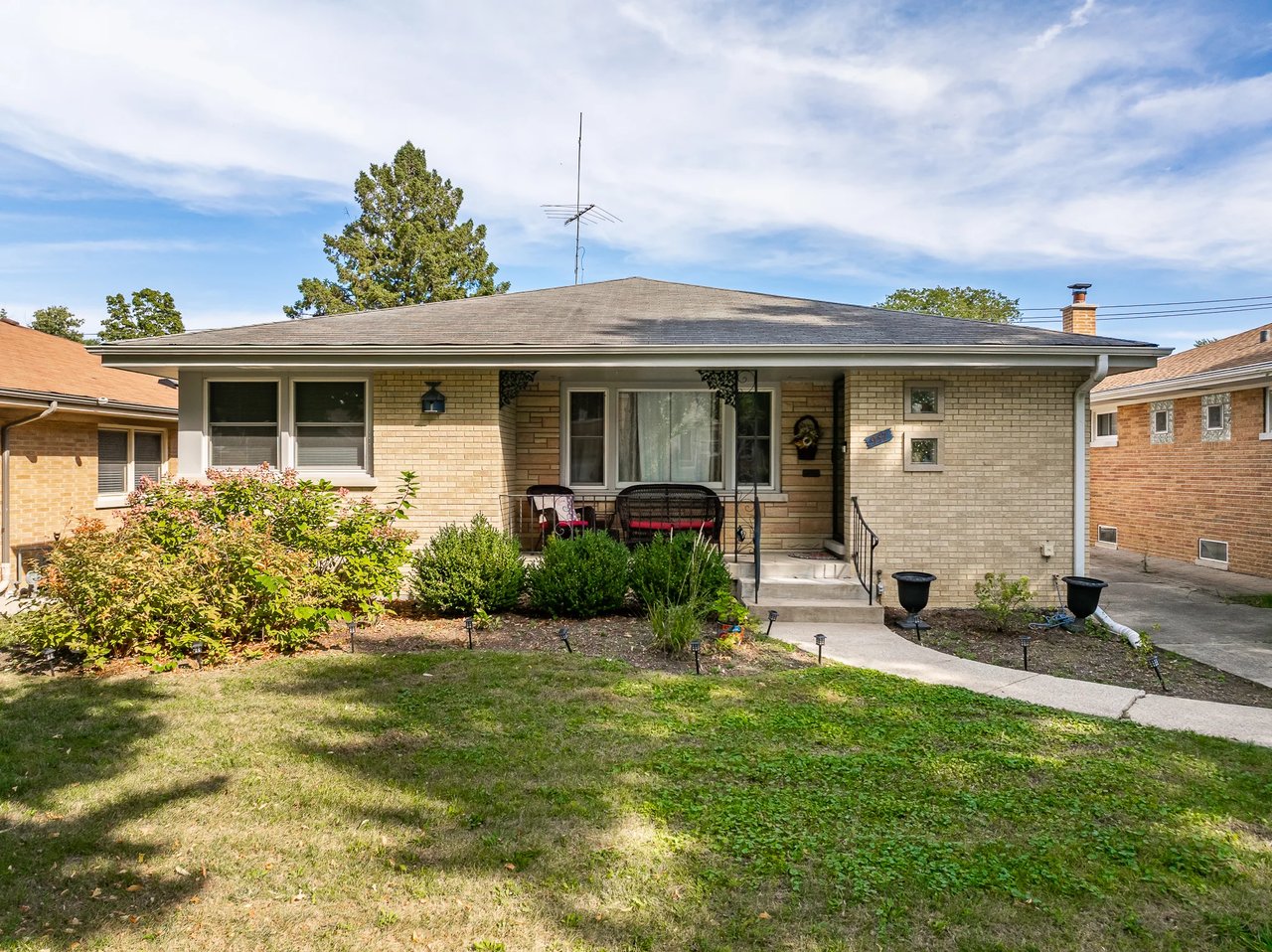 Single-story brick home with a covered entry, front garden, and lawn.