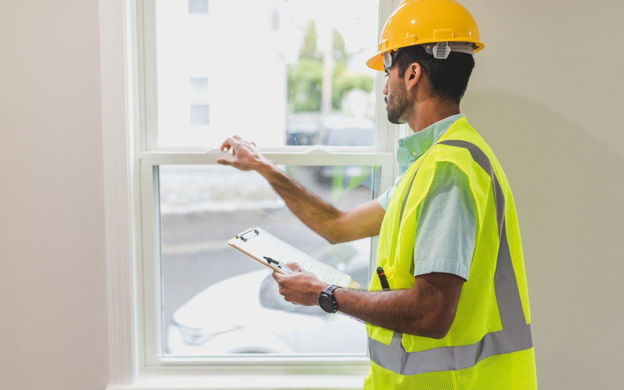 Home inspector checks a window while holding an inspection checklist.