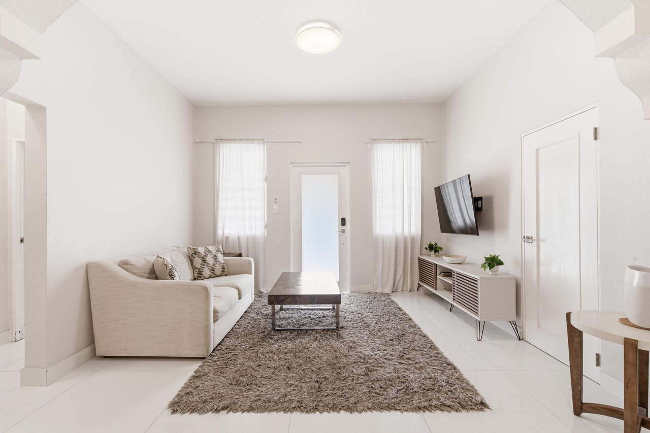 Bright living room with a beige sofa, shag rug, wall-mounted television, and glass-panel entry door.