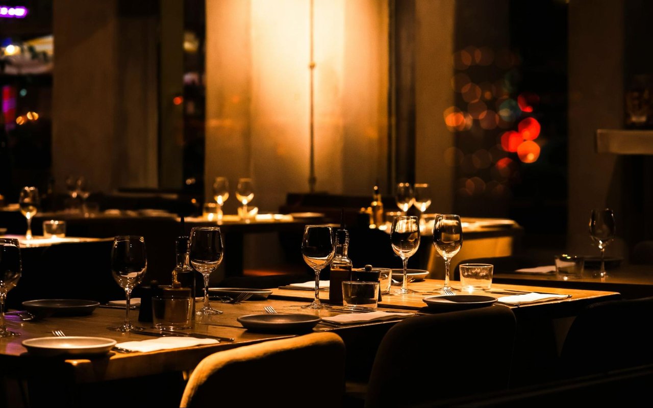 Restaurant dining room with warmly lit tables set with wine glasses and plates.
