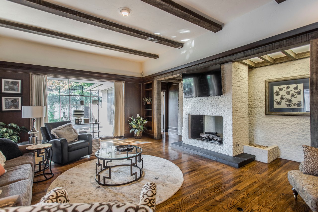 Living room with exposed beams, hardwood floors, and a white stone fireplace.