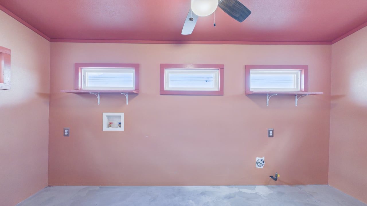 Unfinished laundry room with three high windows, washer hookups, and a bare concrete floor.
