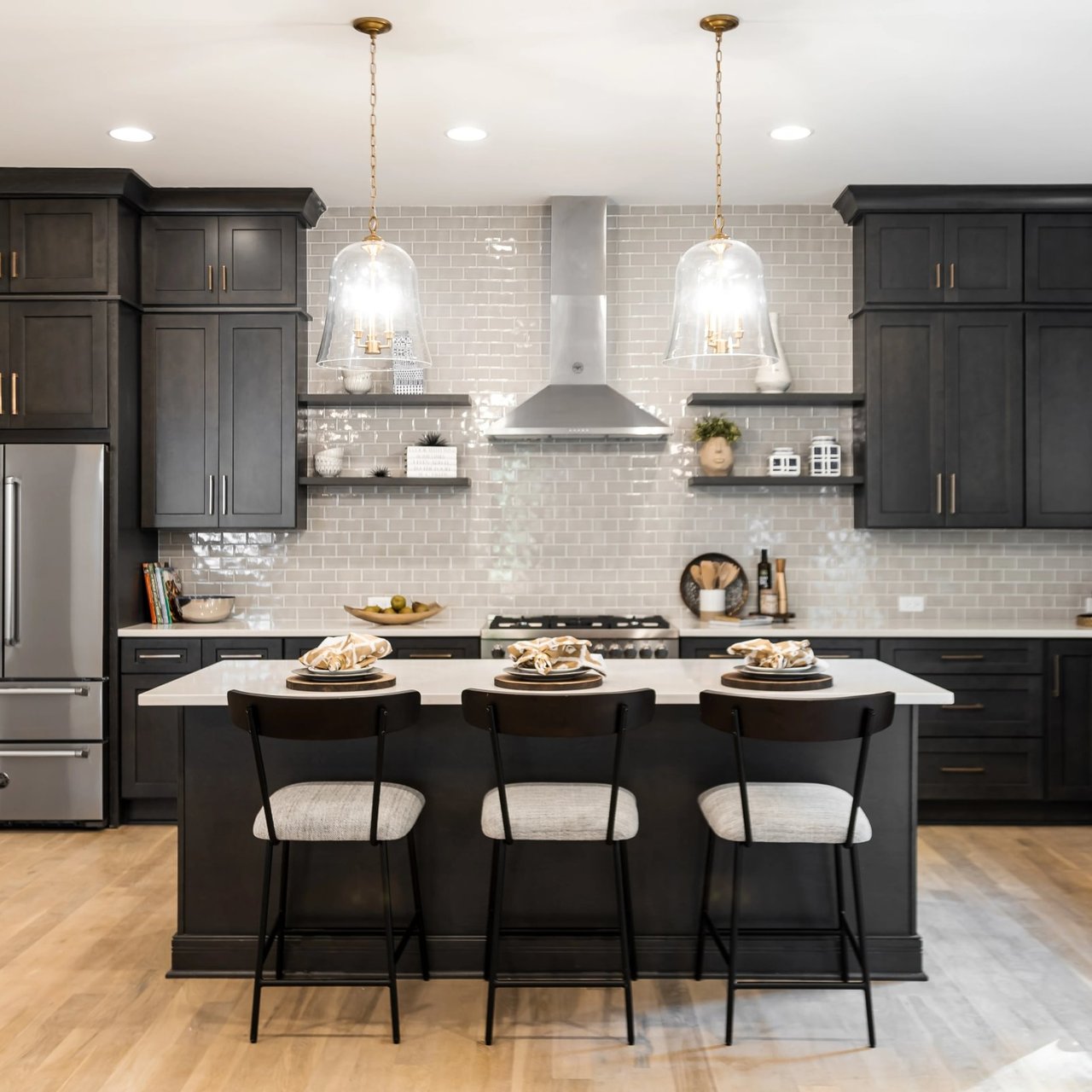 Modern kitchen with dark cabinets, a tiled backsplash, and a large island with three bar stools.