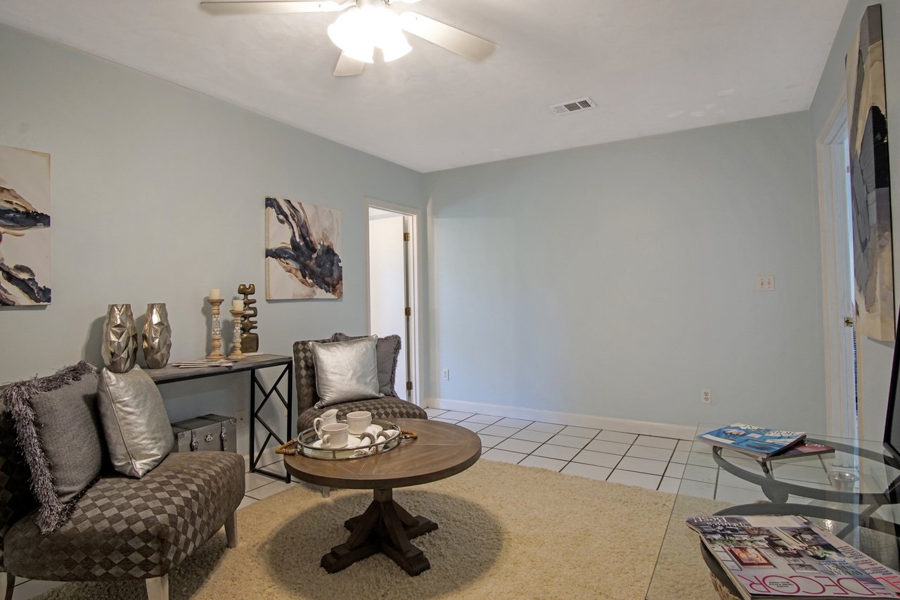 Cozy living room with two patterned chairs, a wooden coffee table, and silver decor on a console table. Abstract paintings adorn light blue walls.