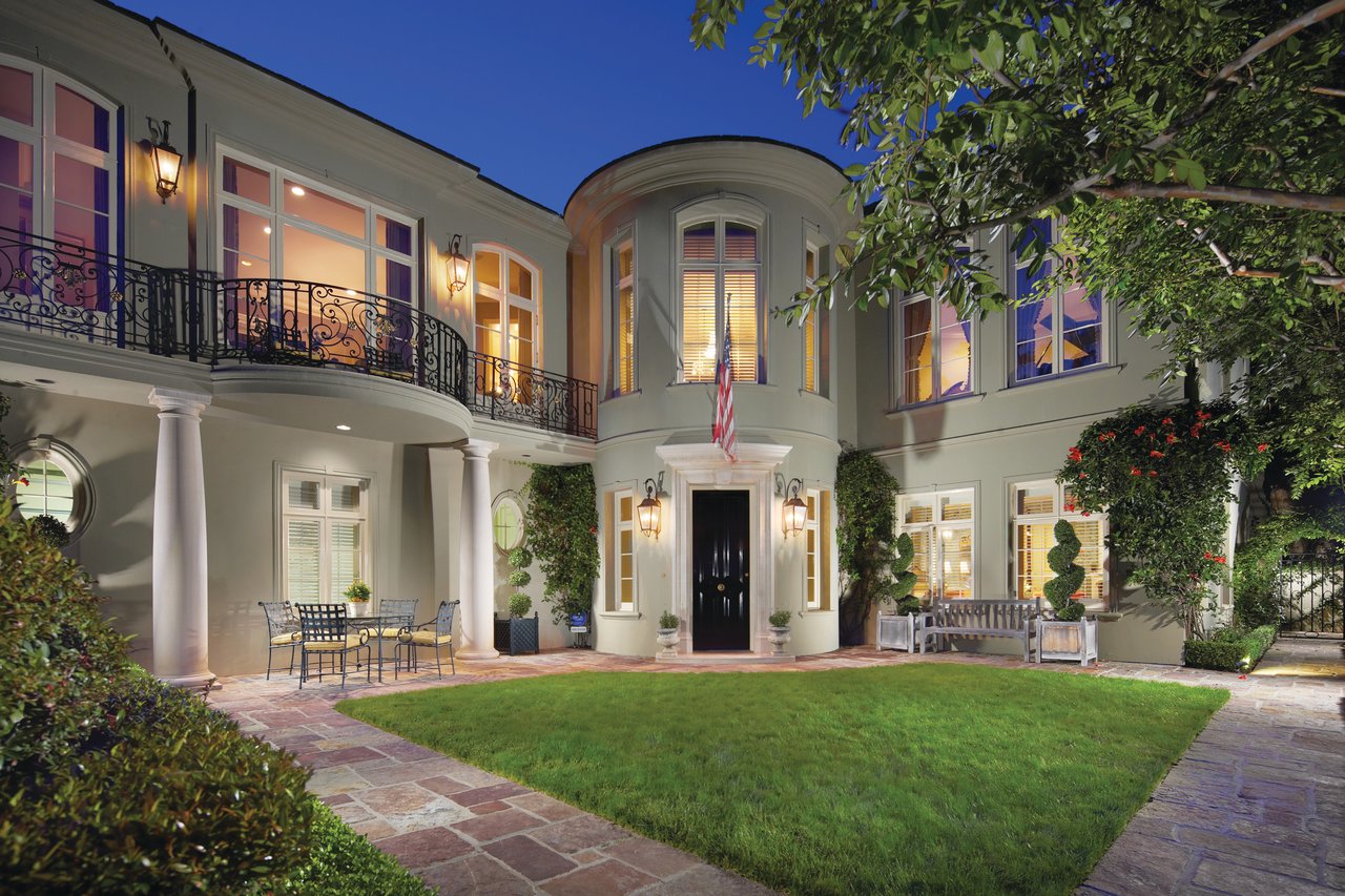 Two-story home with a curved entry, iron balconies, and illuminated windows at dusk.
