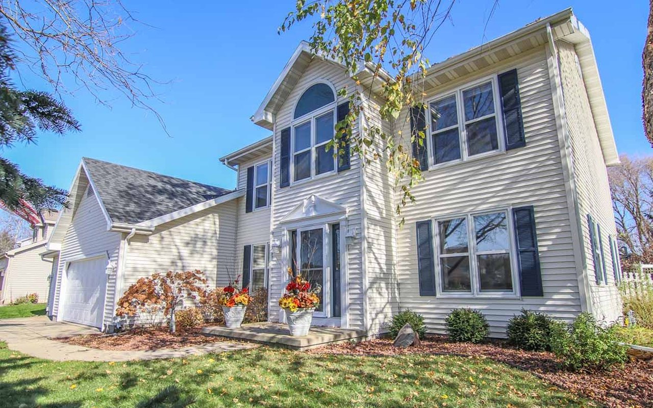 Two-story colonial home with dark shutters, an attached garage, and flower planters at the entrance.