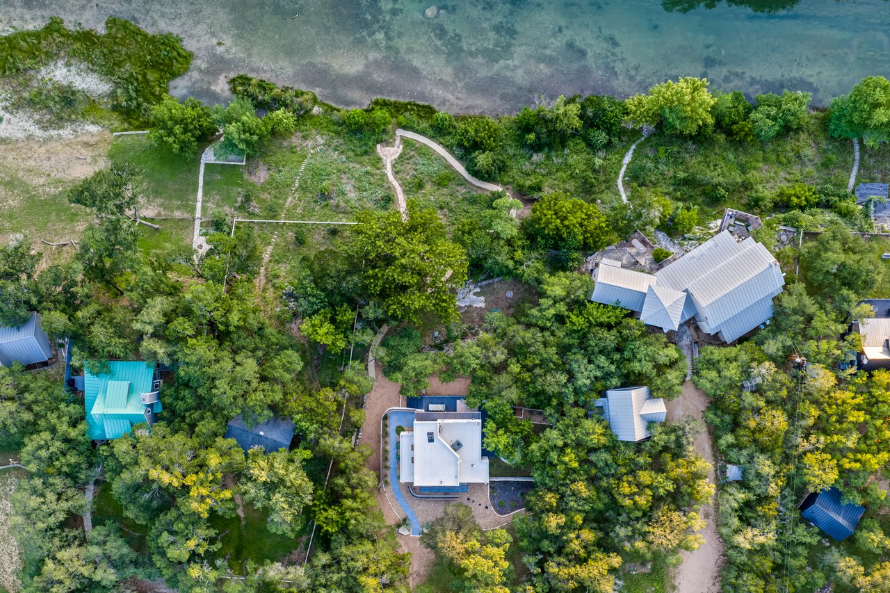 Aerial view of a wooded riverfront property with homes, garden paths, and shoreline.