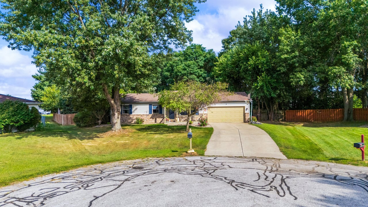 Single-story ranch home with an attached garage, broad driveway, and mature shade trees.