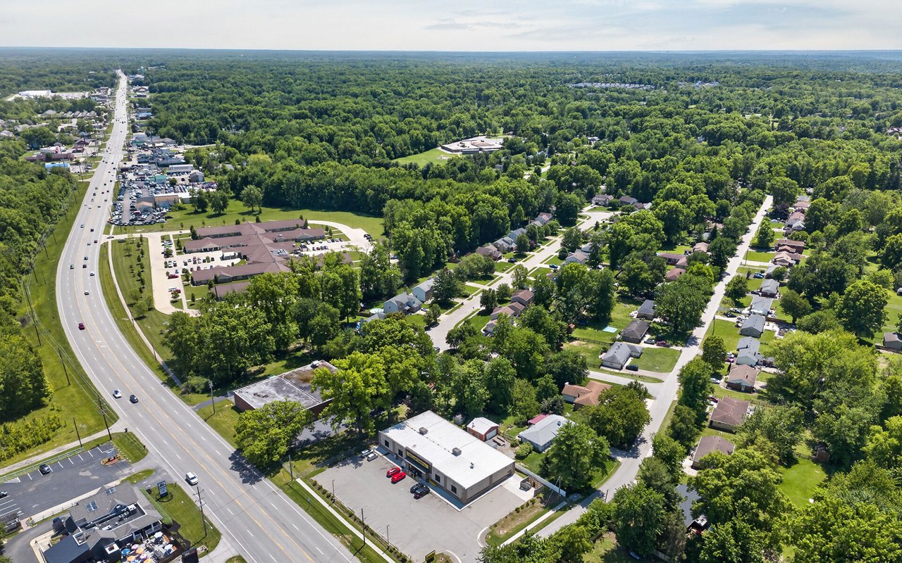 Aerial view of a multifamily complex beside a highway, surrounded by tree-lined residential streets.