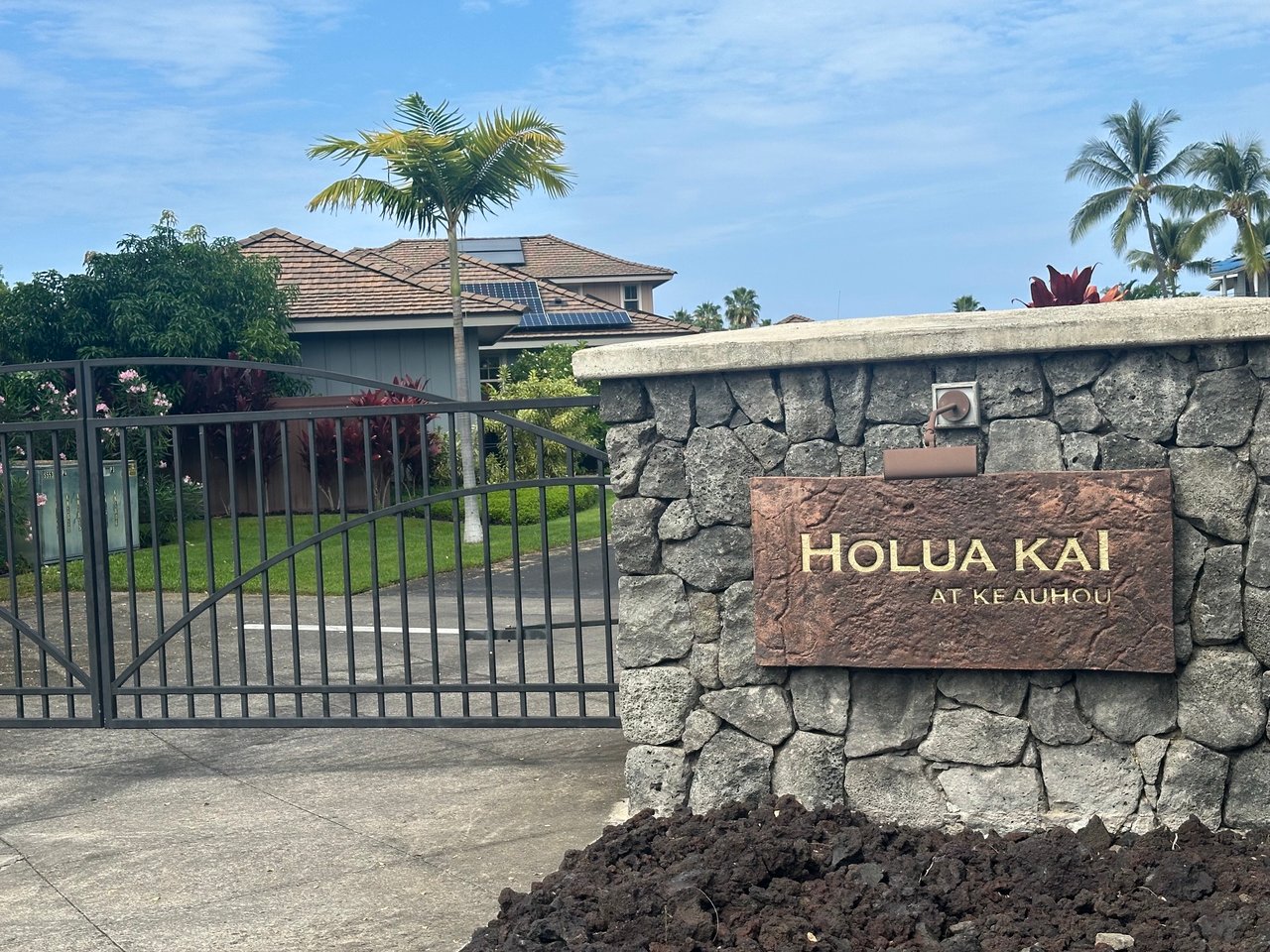Holua Kai at Keauhou entrance sign beside a black metal gate and tropical landscaping.