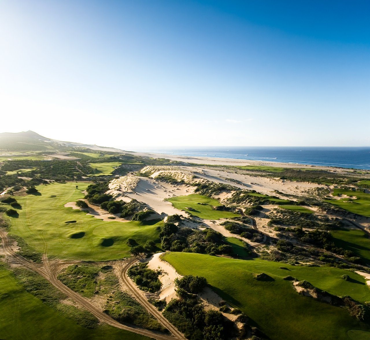 Coastal golf course winds through sandy dunes beside a beach and ocean.