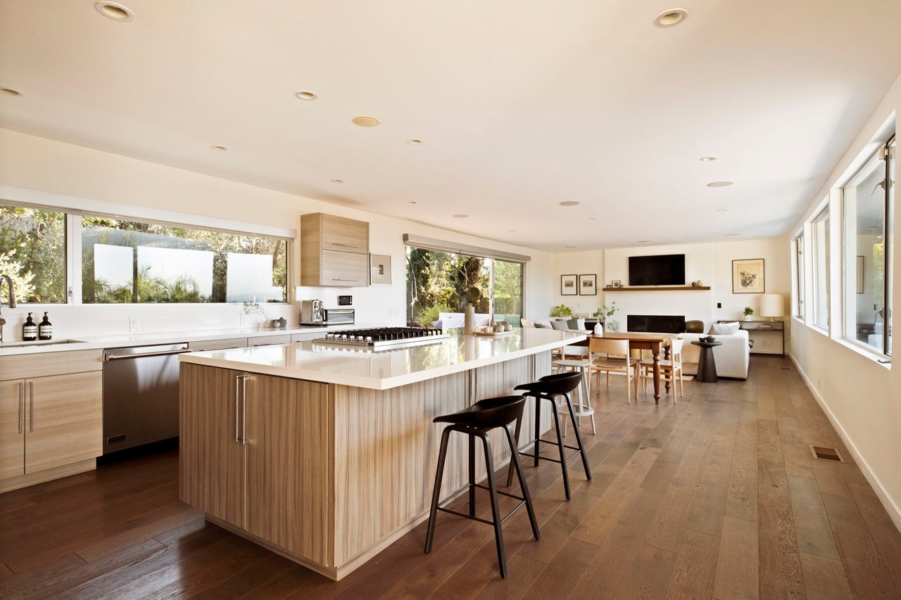 Open-plan kitchen with a large white island and bar stools, dining area, and living room beyond.