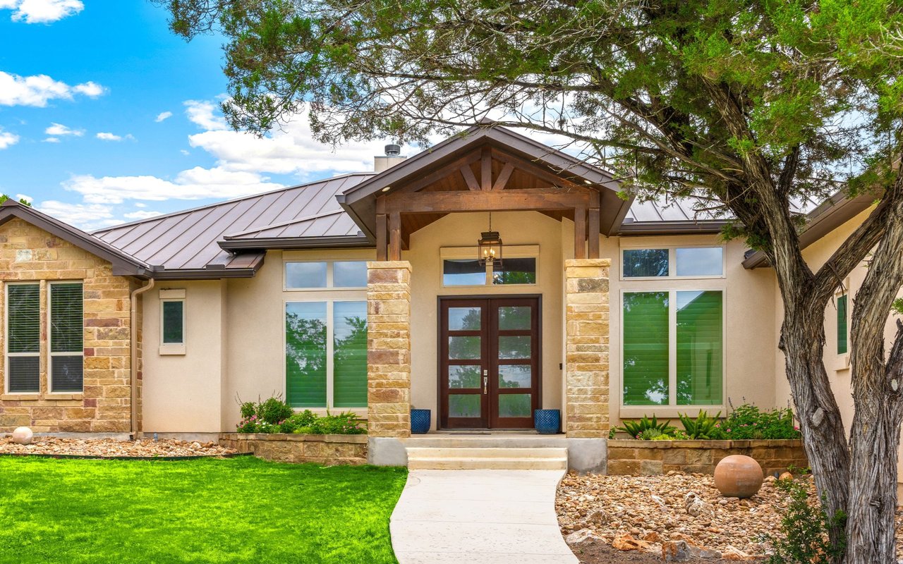 Single-story home with a timber entrance gable, stone columns, and a curved walkway through the lawn.