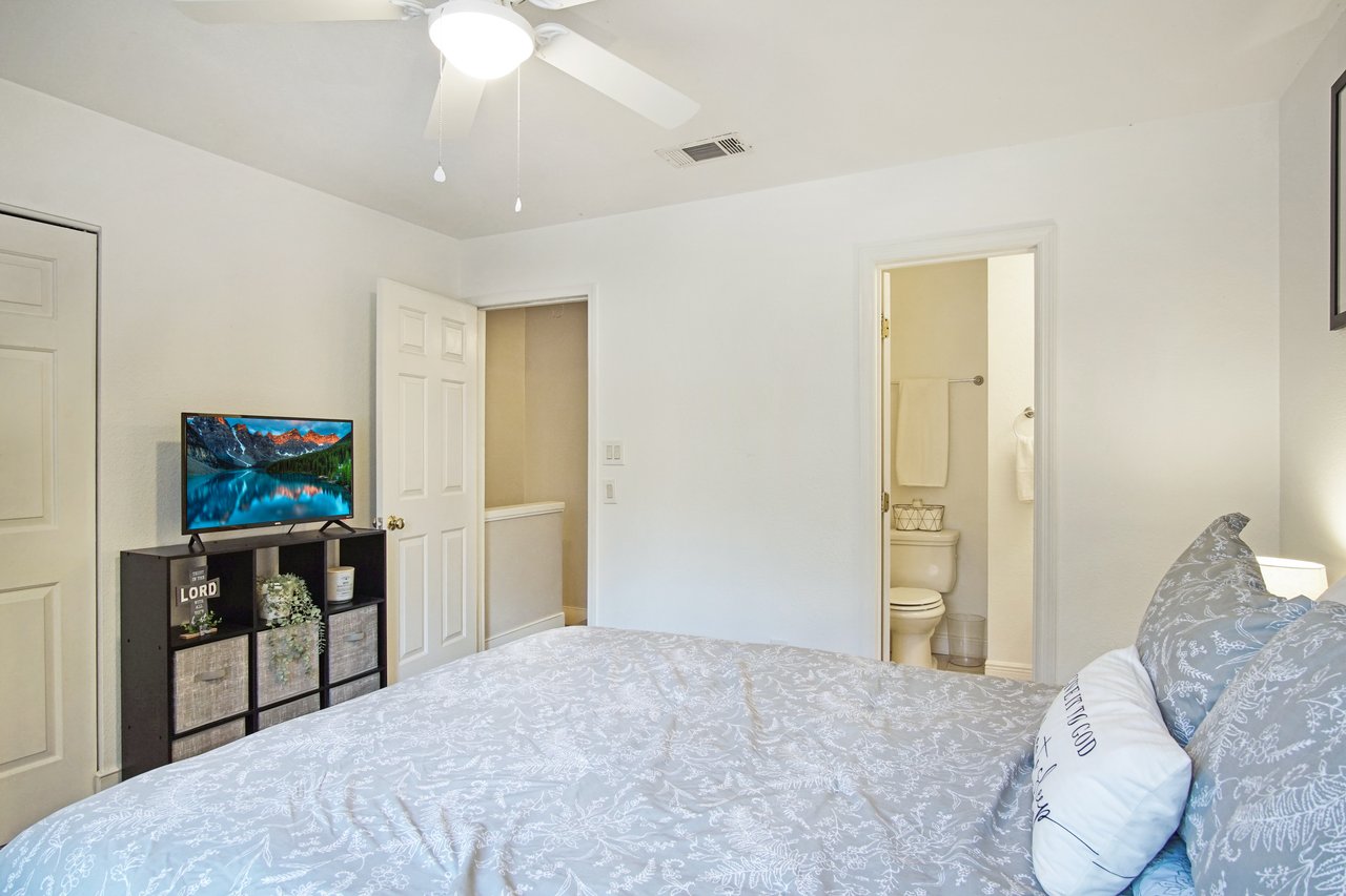 A cozy bedroom features a neatly made bed with a patterned duvet. A TV displays a scenic landscape on a cube shelf unit beside a white closet. Soft, warm lighting creates a calm atmosphere.