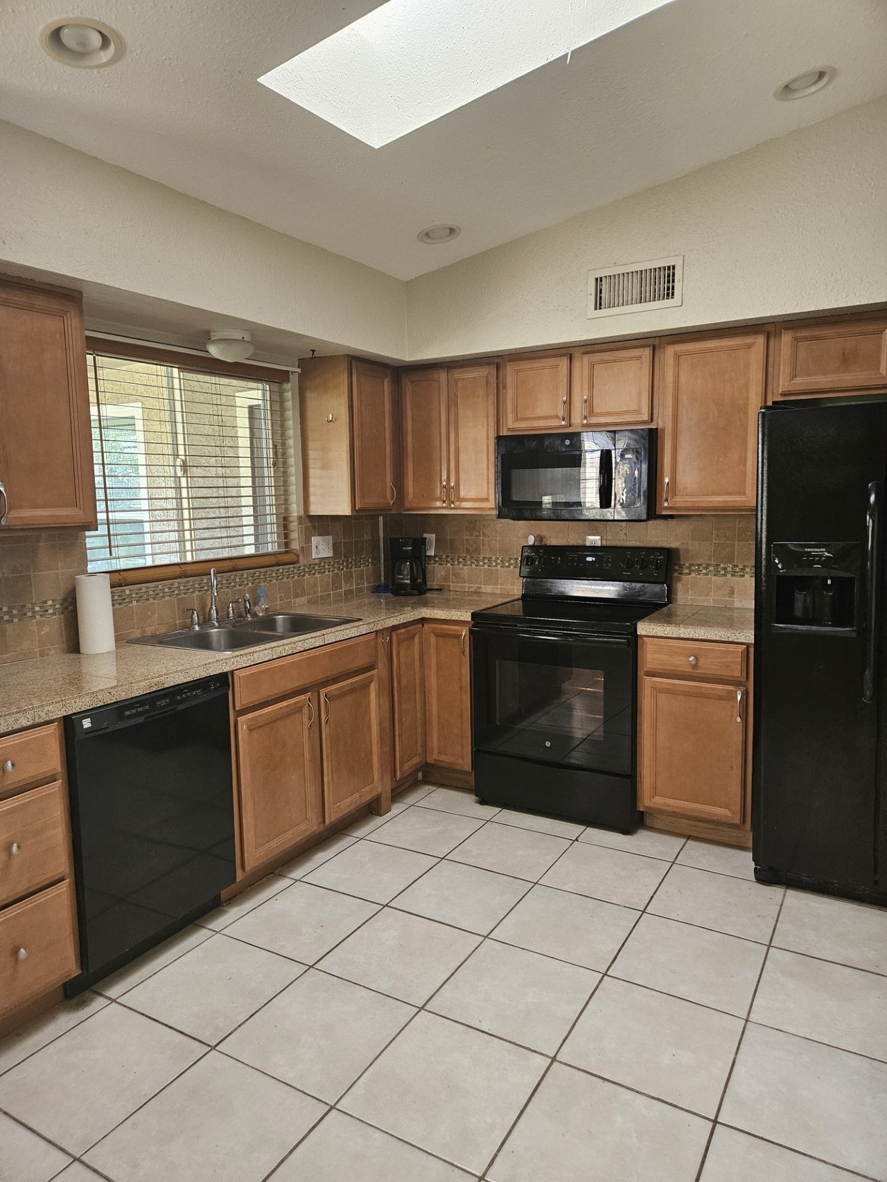 Kitchen with wood cabinets, tiled counters and backsplash, black appliances, and a skylight.