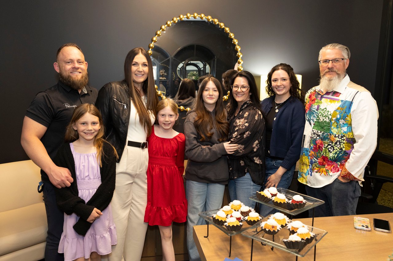 Eight people pose together at an indoor open house beside trays of cupcakes.