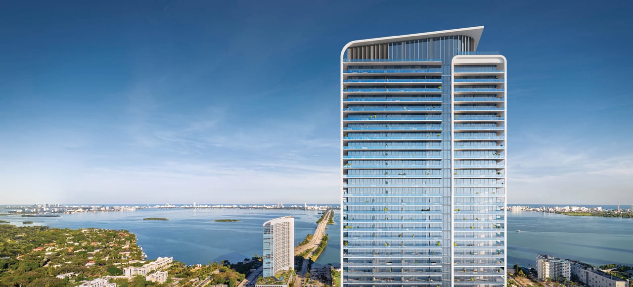Modern glass residential tower overlooking Biscayne Bay, with Miami’s skyline in the distance.