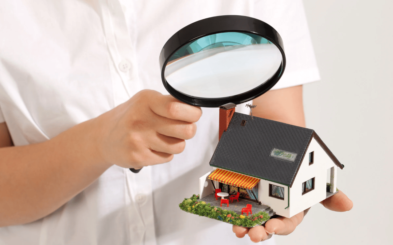 A person examines a miniature house with a magnifying glass.