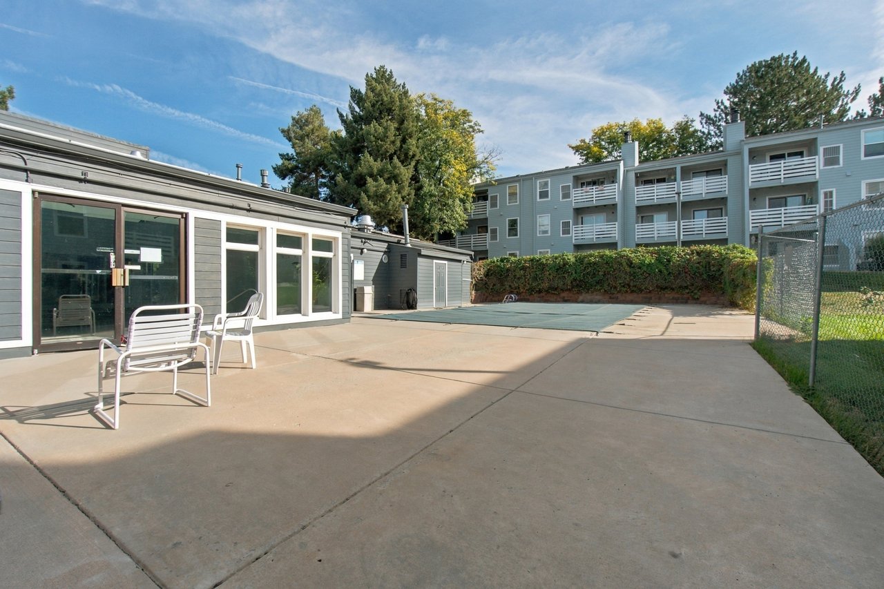 Apartment community pool courtyard with a covered pool, concrete patio, and metal chairs.