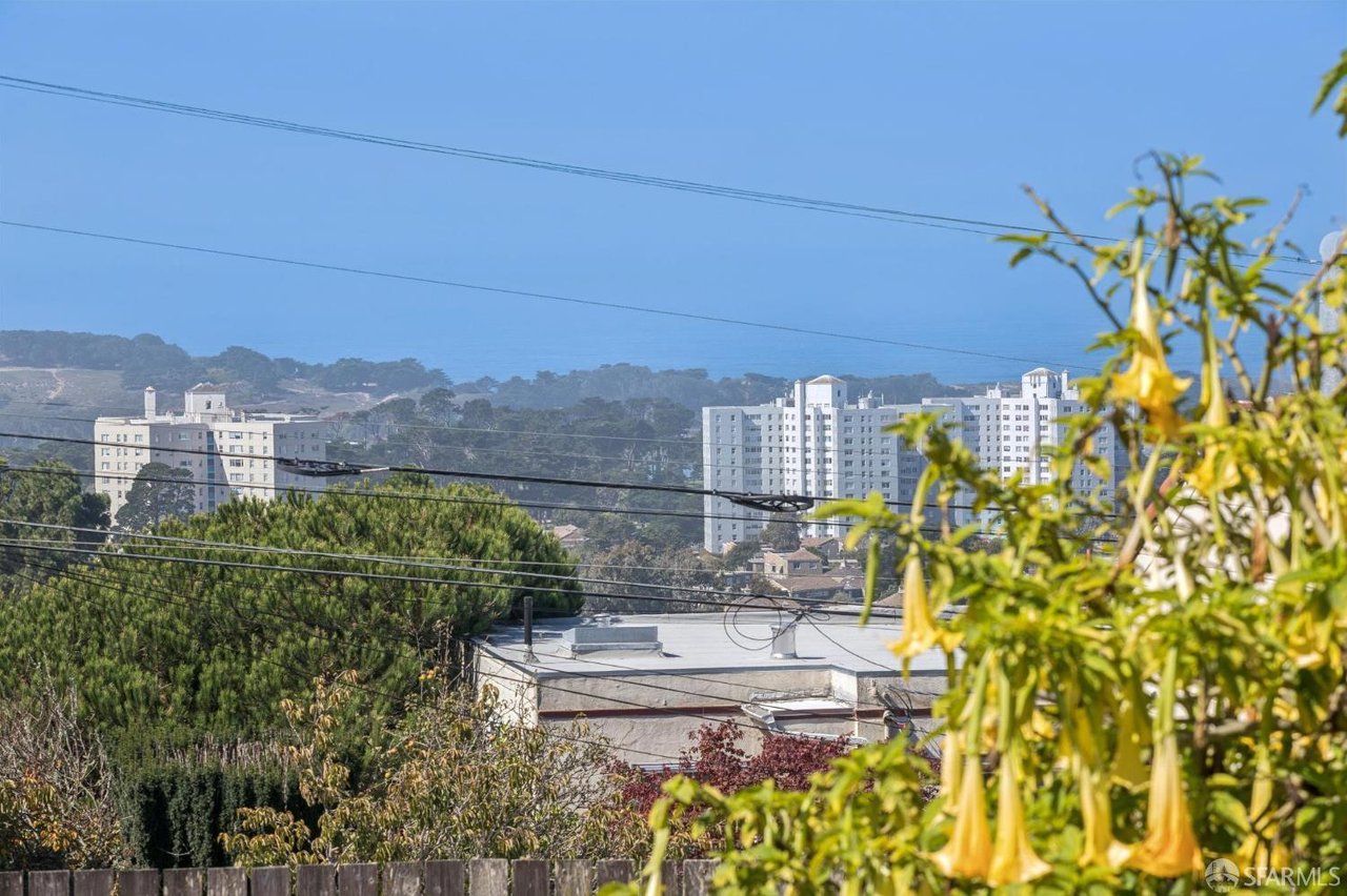 City skyline beyond rooftops and trees, framed by yellow trumpet-shaped flowers.
