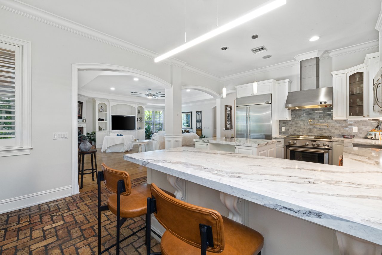 Open kitchen with a large marble island, stainless steel appliances, and an adjoining living room.