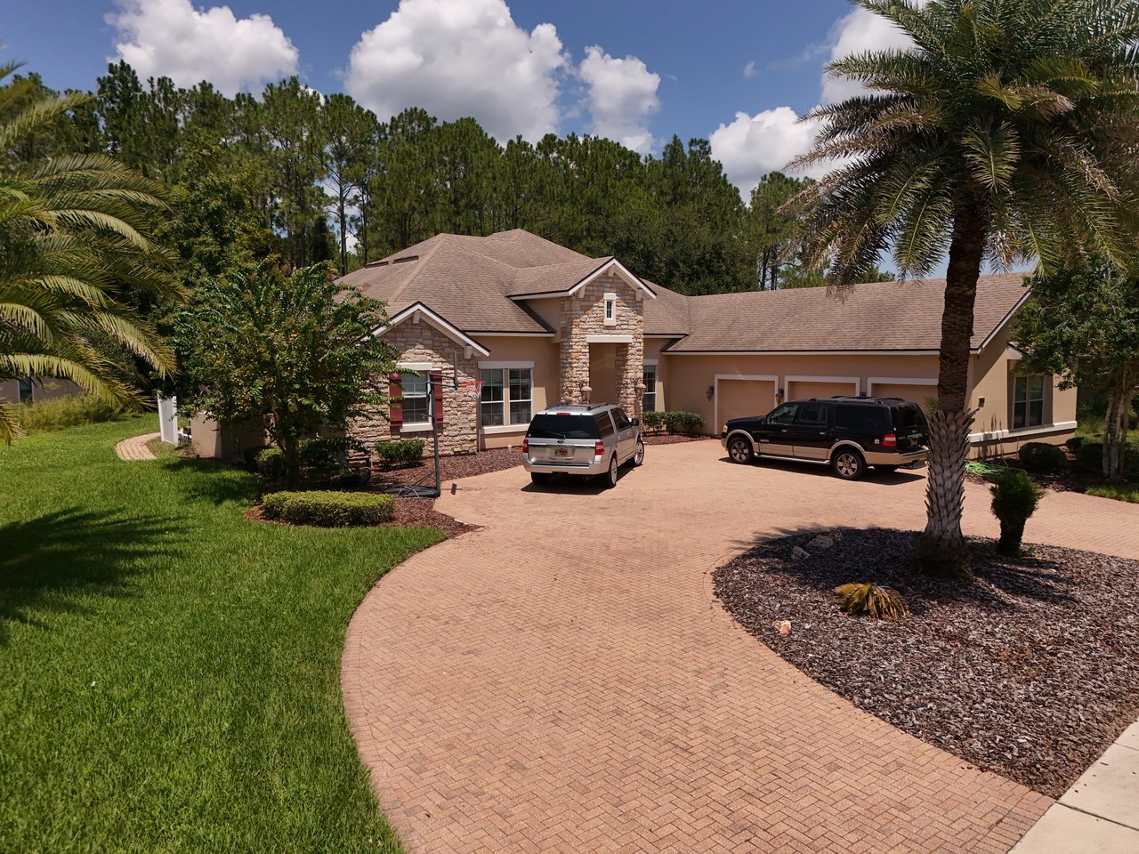 Single-story home with stone accents, a three-car garage, and a curved brick-paver driveway.