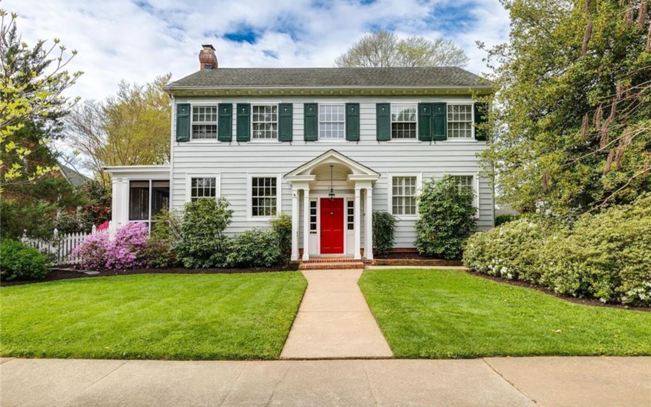 White two-story house with green shutters, red front door, and landscaped lawn.