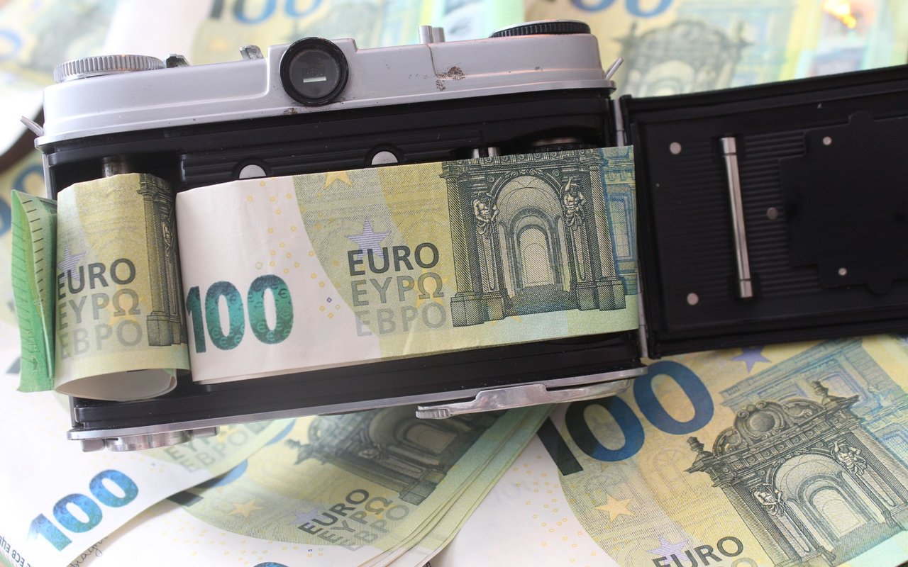 Vintage camera loaded with €100 euro notes, resting on more banknotes.
