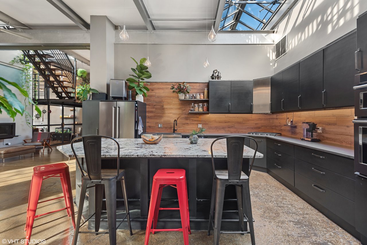 Modern kitchen with a marble island, dark cabinets, wood backsplash, and skylight.