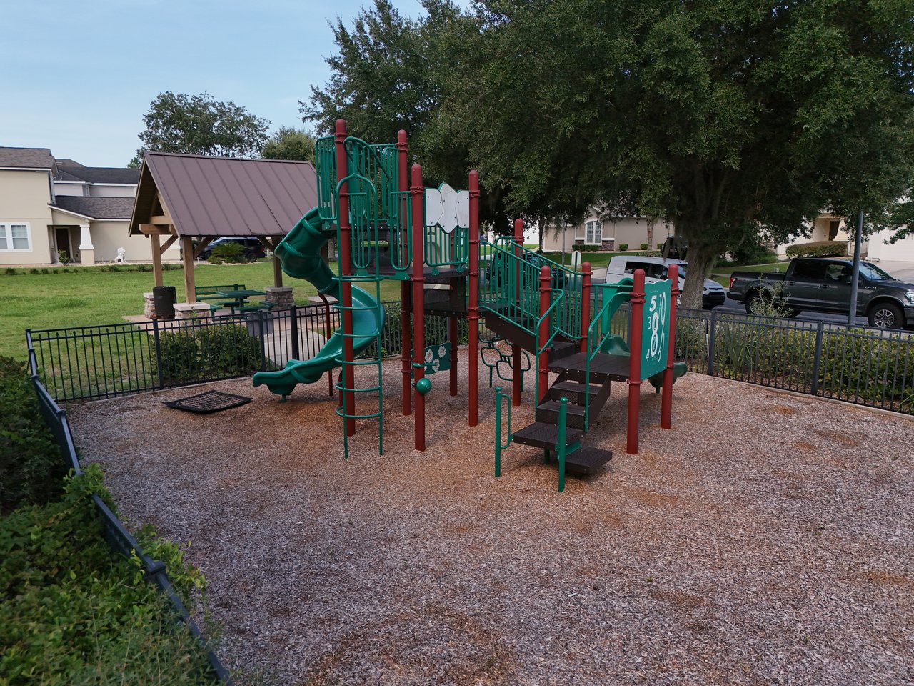 Neighborhood playground with green slides and climbing equipment beside a covered picnic area.