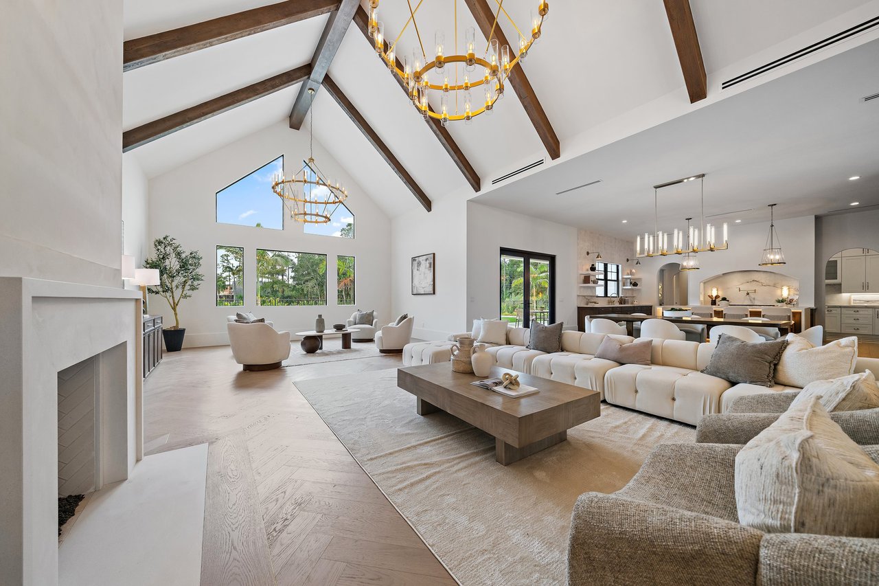 Living room with vaulted wood-beam ceiling, gold chandelier, cream sofas, and white fireplace.