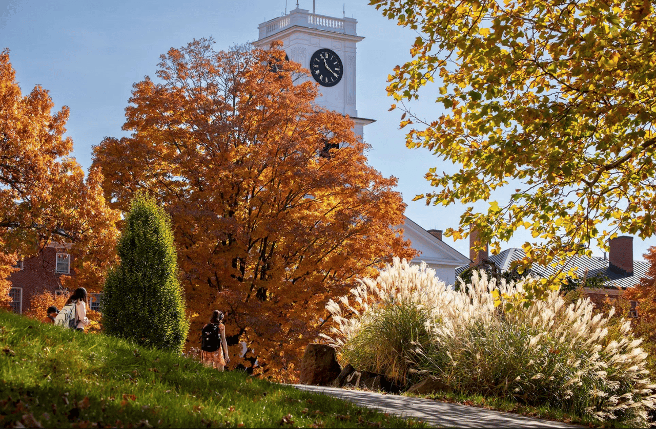 Campus clock tower above a walkway framed by colorful autumn trees and students.