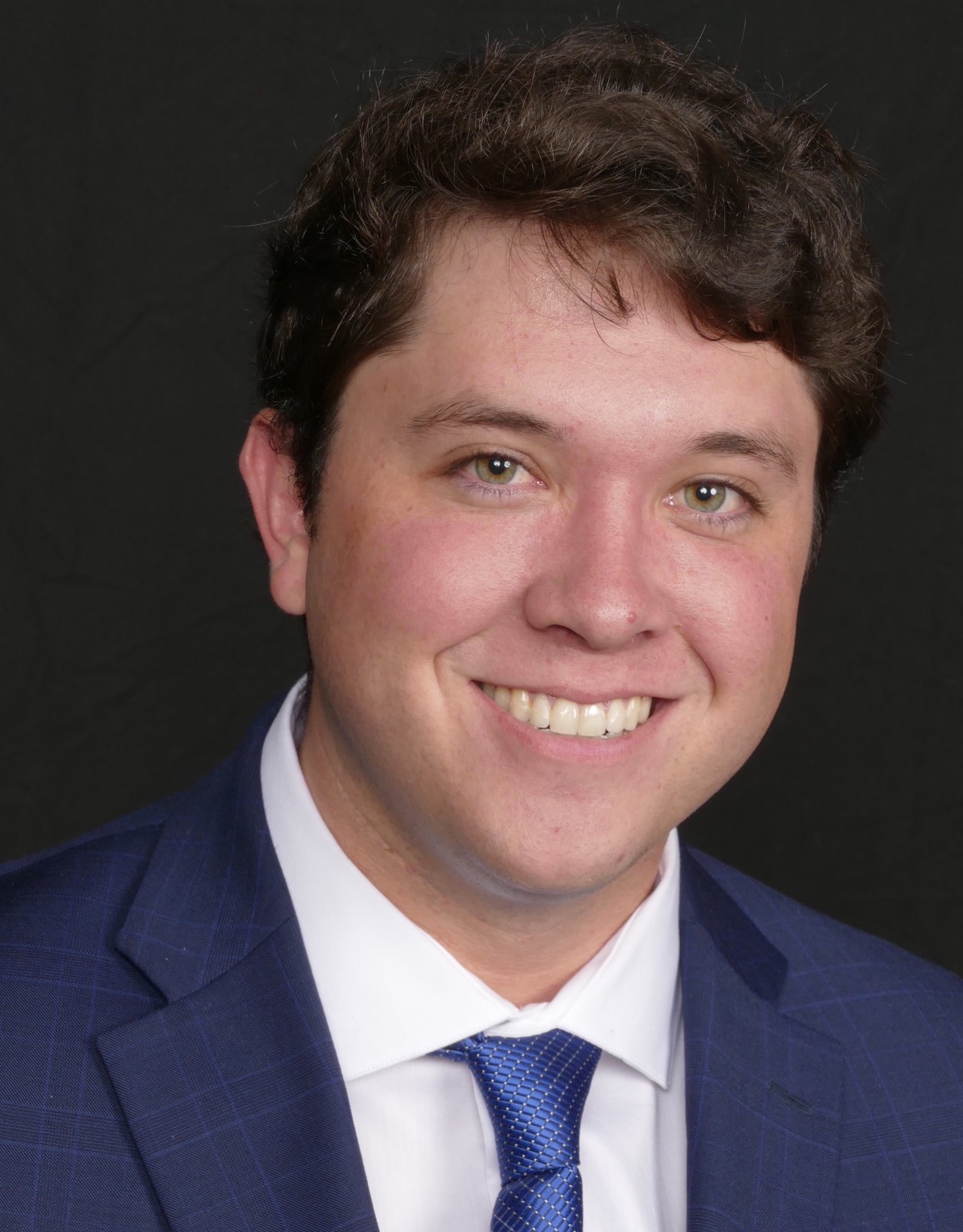 John Fenton smiling in a blue suit, white shirt, and patterned blue tie.