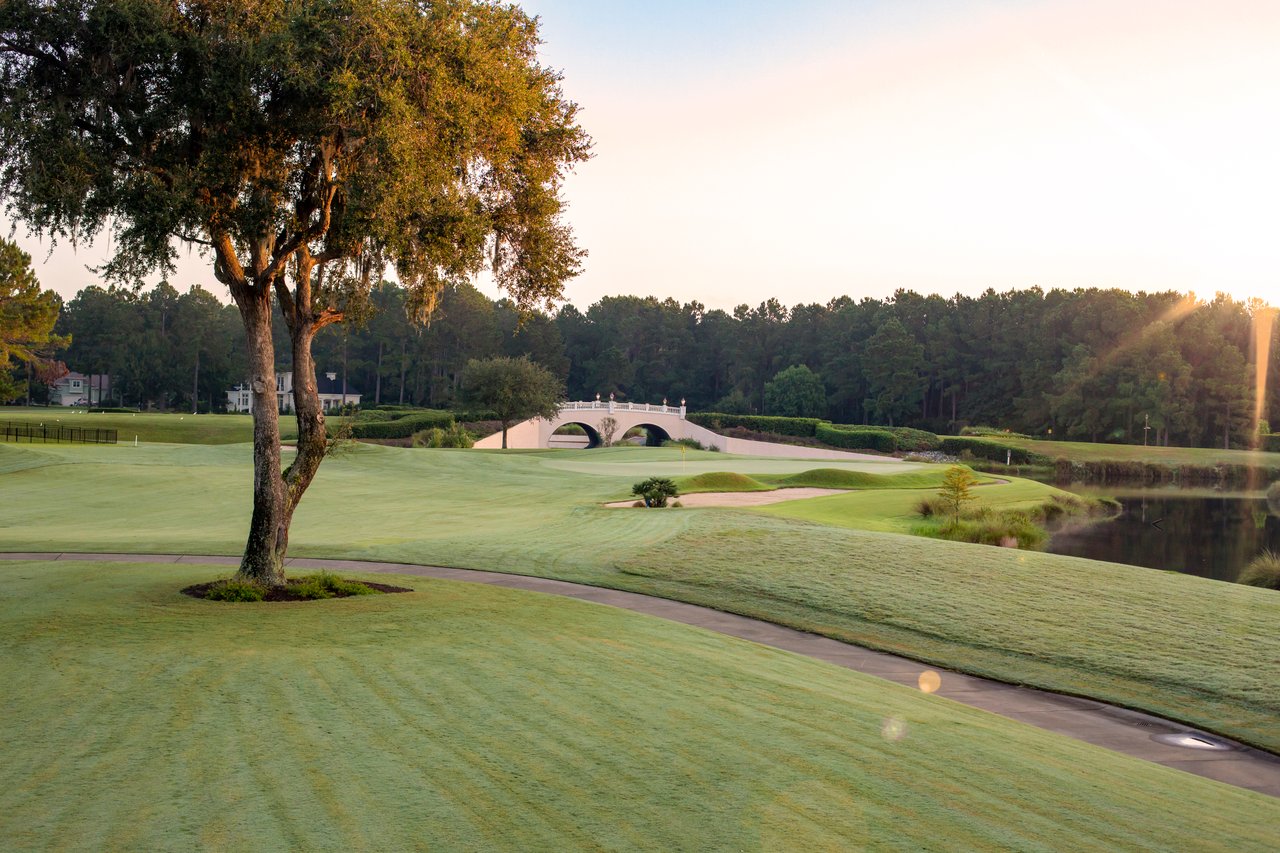 Hampton Hall golf course with a white arched bridge, pond, and moss-draped oak.