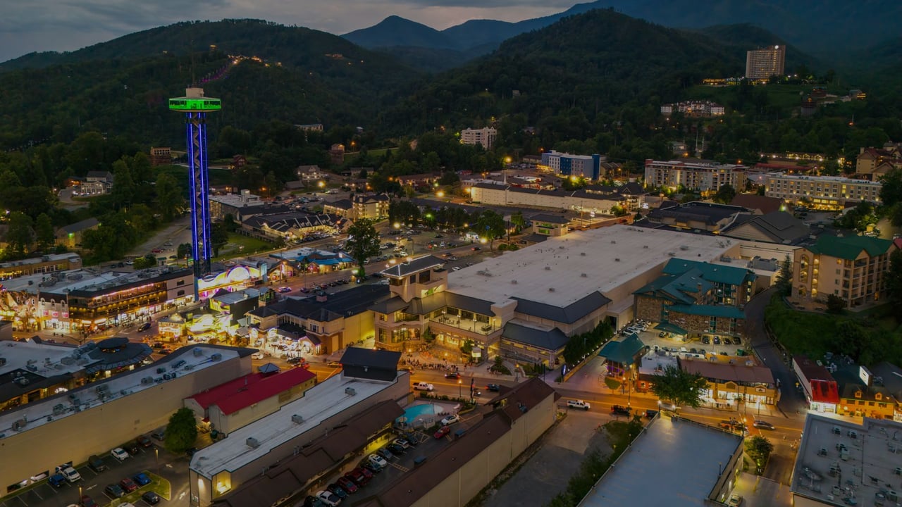 Downtown Gatlinburg at dusk, with the illuminated Space Needle beneath forested mountain ridges.