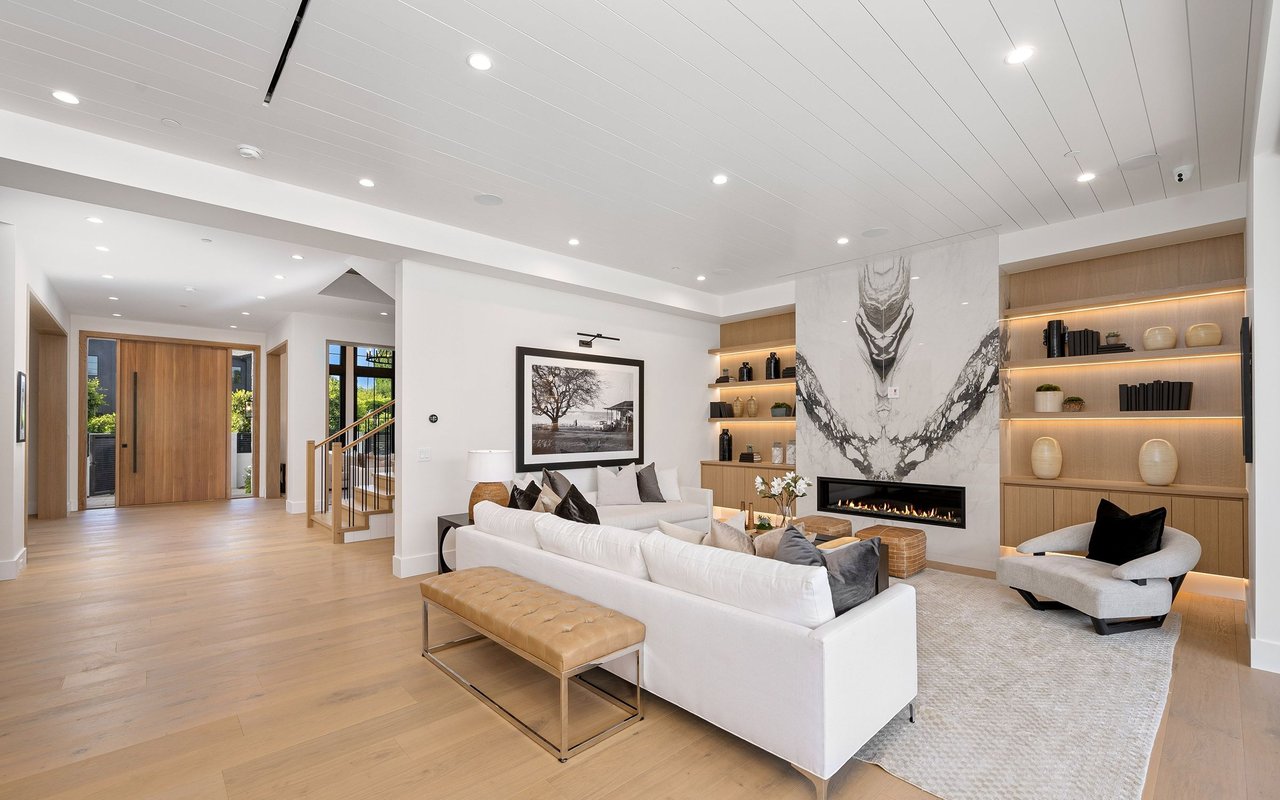 Modern living room with a white sectional, illuminated built-in shelves, and a dramatic marble fireplace wall.