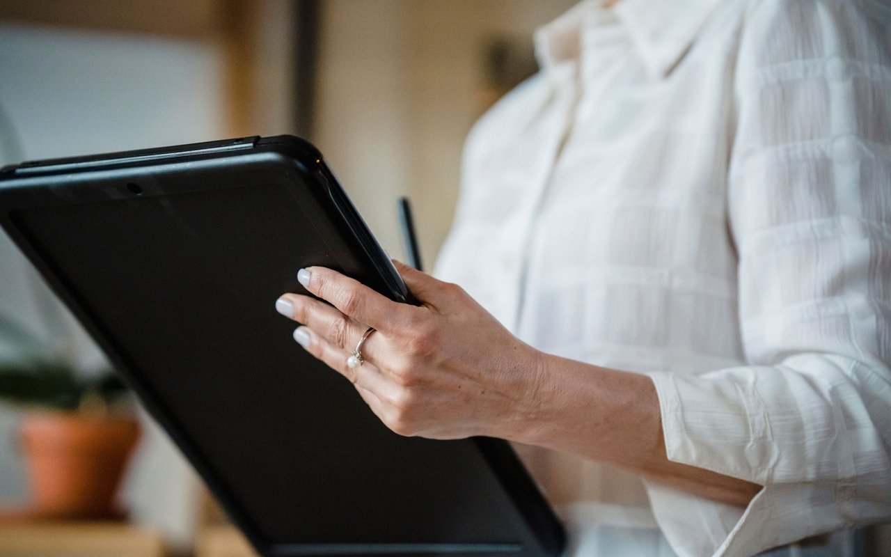Person in a white blouse holding a black tablet indoors.