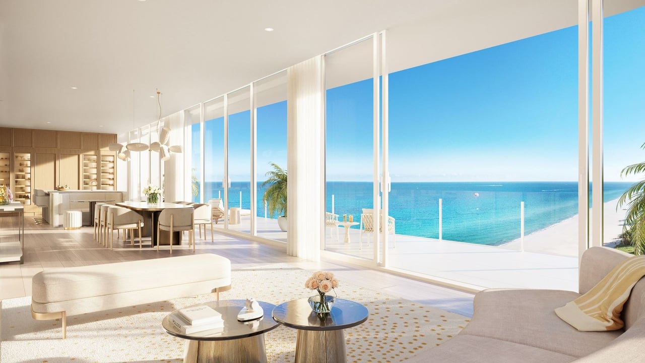 Furnished living and dining area with floor-to-ceiling windows overlooking the ocean and beach.