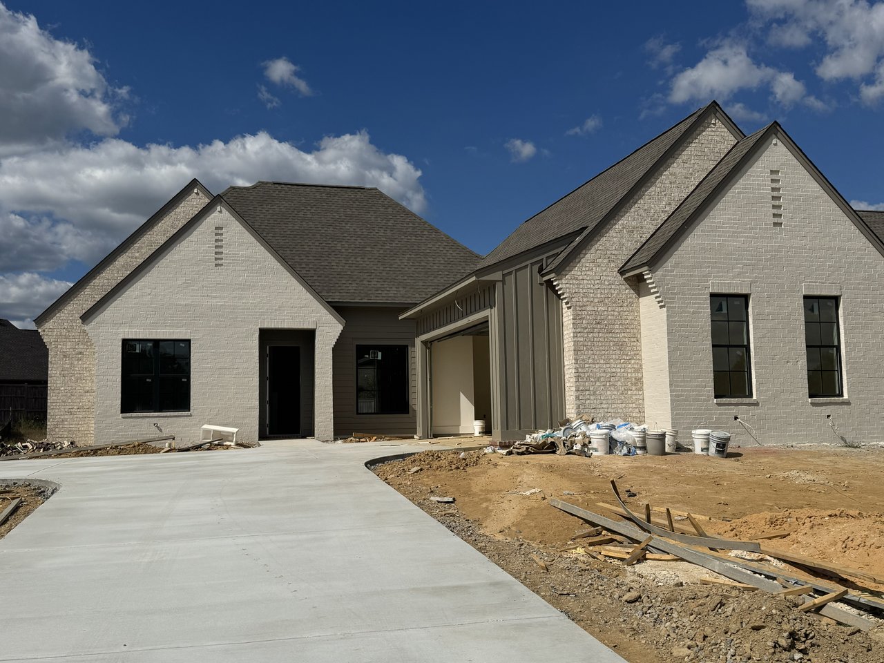 Newly built brick house with steep gables, a concrete driveway, and unfinished landscaping.