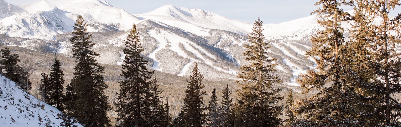 Snow-covered Breckenridge mountain slopes and wooded valleys framed by evergreen trees.