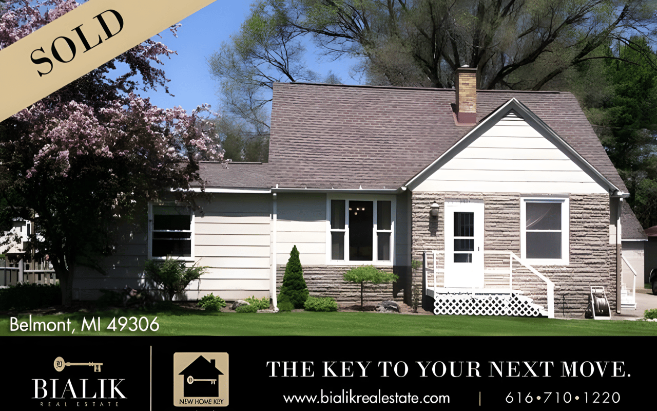 Belmont home marked sold, with a stone facade, white siding, and flowering trees.