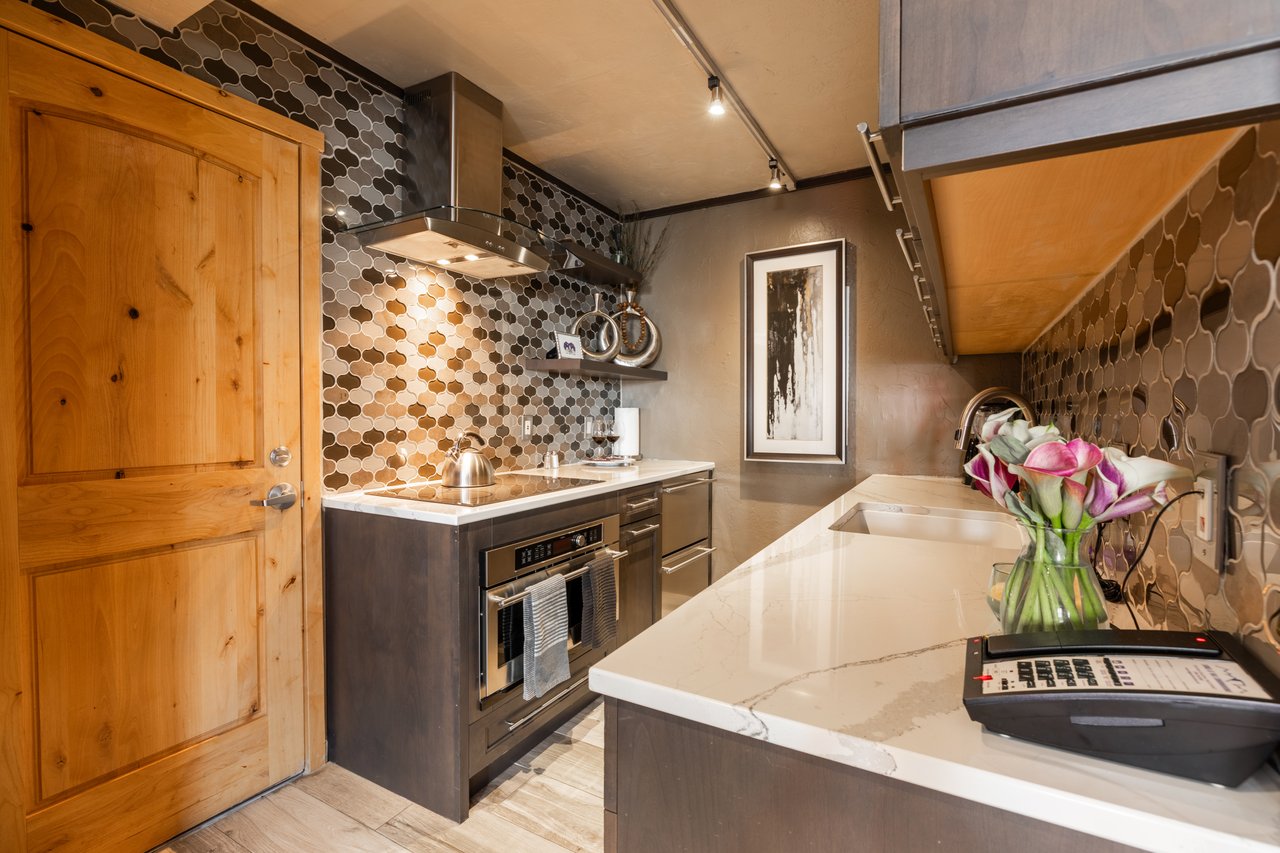 Kitchen with white marble island, patterned tile backsplash, stainless steel appliances, and warm wood cabinetry.