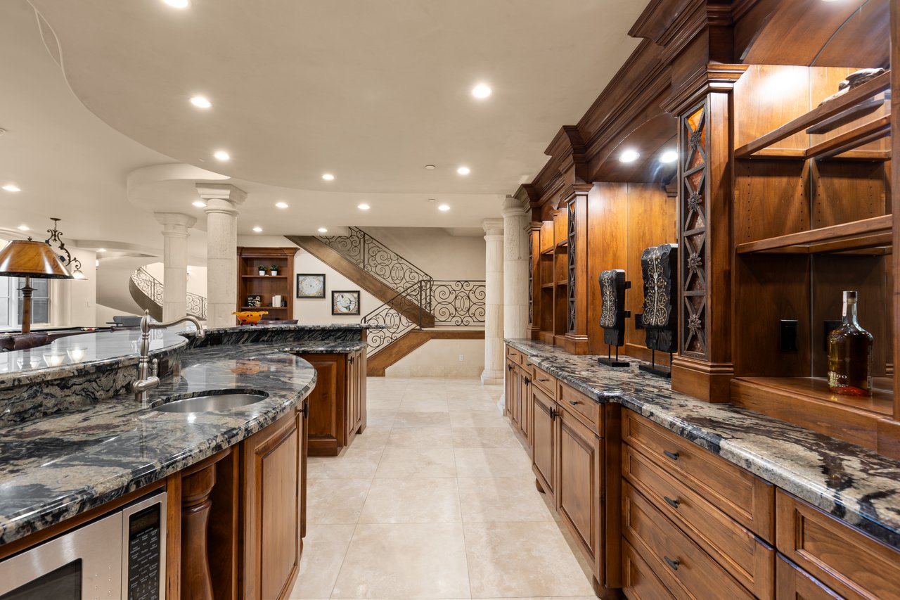 Kitchen with curved granite counter, sink, extensive wood cabinetry, and a decorative staircase.
