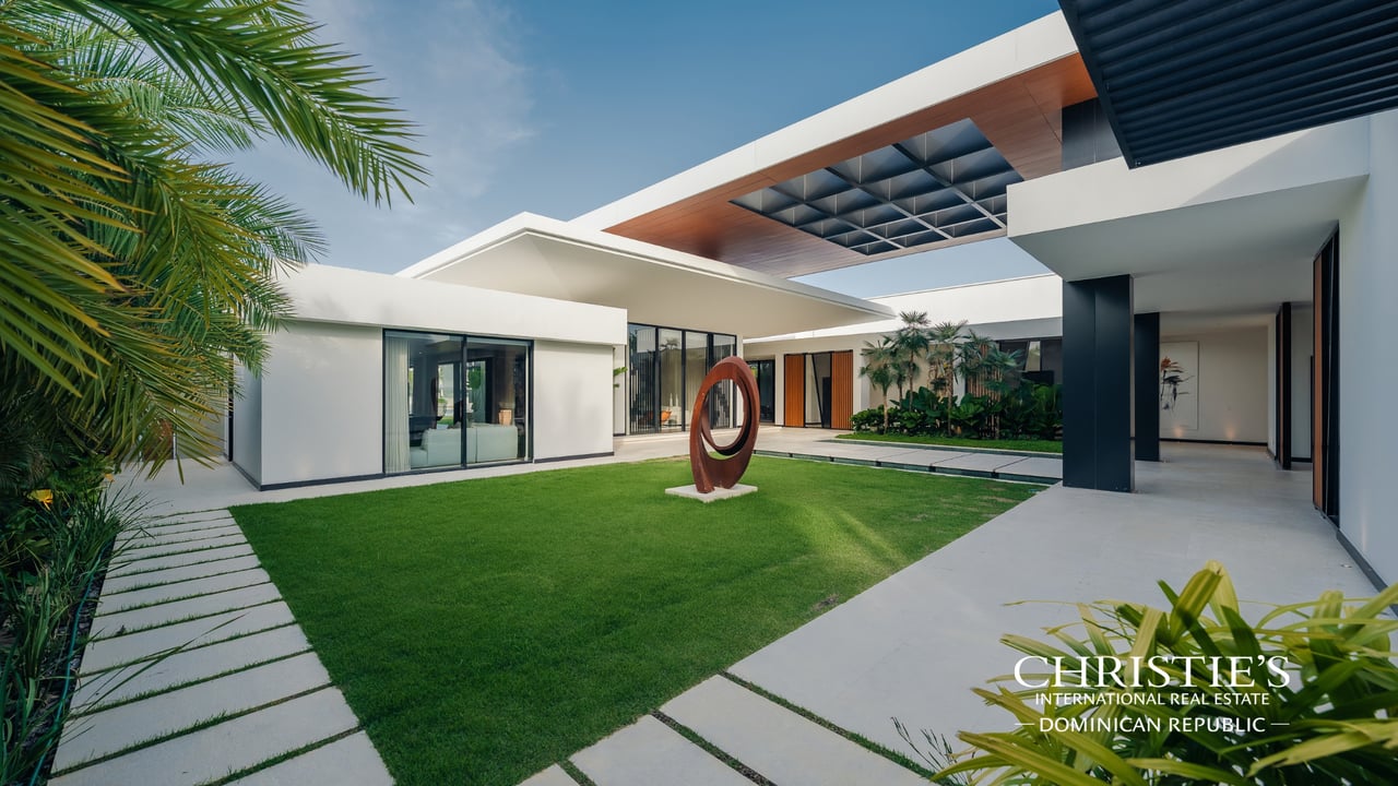 Modern villa courtyard with a green lawn, palm trees and an abstract sculpture.