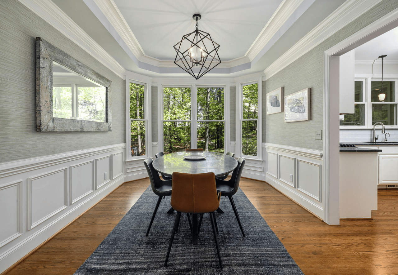 Elegant dining room with gray textured wallpaper, tray ceiling, and a large bay window overlooking trees.